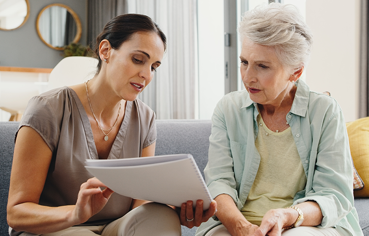 A daughter and elderly mom discuss a piece of paper the daughter is holding.